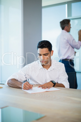 Business executive writing on notebook in conference room