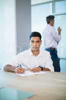 Thoughtful business executive writing on notebook in conference room