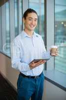 Business executive using digital tablet while having coffee in office corridor