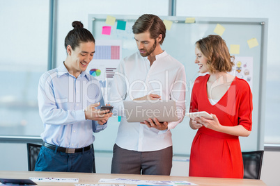 Smiling business colleagues using mobile phone, digital tablet and laptop