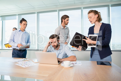 Colleagues with document, digital tablet and mobile phone talking to frustrated man