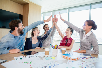 Team of business executives giving high five in conference room