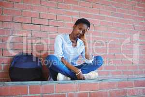 Sad schoolgirl sitting against brick wall