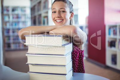 Portrait of happy schoolgirl leaning of stacked books in library