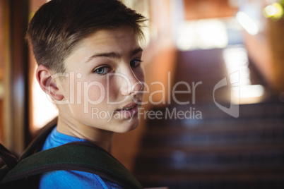 Schoolboy standing with schoolbag near staircase at school