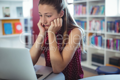 Sad schoolgirl looking at laptop in library