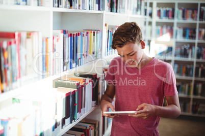 Happy schoolboy using digital tablet in library