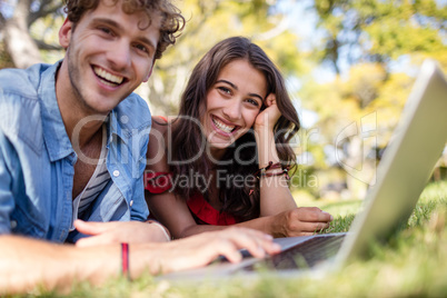 Couple lying on grass and using laptop