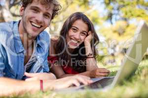 Couple lying on grass and using laptop