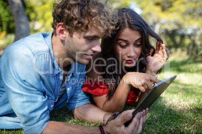 Couple lying on grass and using digital tablet