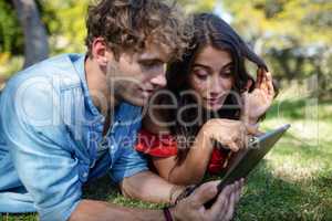 Couple lying on grass and using digital tablet