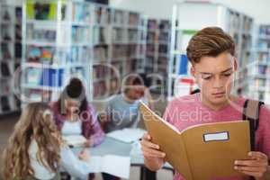 Schoolboy reading book with his classmates studying in background