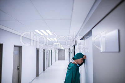 Tensed female surgeon leaning on wall in corridor