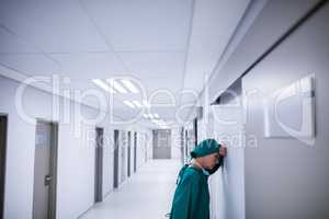 Tensed female surgeon leaning on wall in corridor