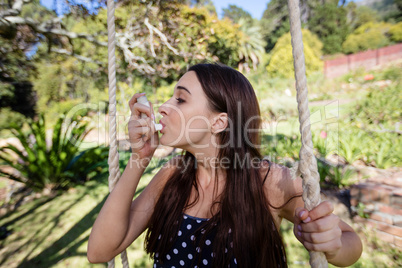 Woman sitting on swing using an asthma inhaler