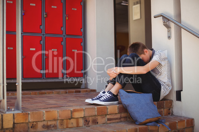 Sad schoolboy sitting on staircase