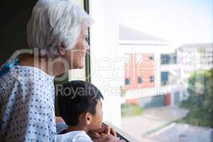 Senior patient and boy looking out from the window