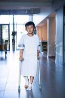 Boy patient walking with crutches in corridor