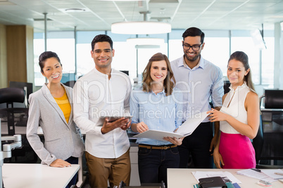 Smiling business colleagues discussing over clipboard and digital tablet at desk in office