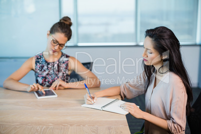 Business colleagues writing on notepad and using digital tablet in conference room