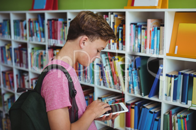 Attentive schoolboy using digital tablet in library