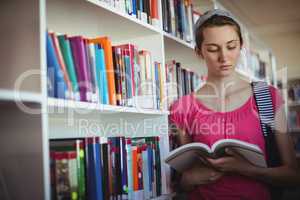 Attentive schoolgirl reading book in library