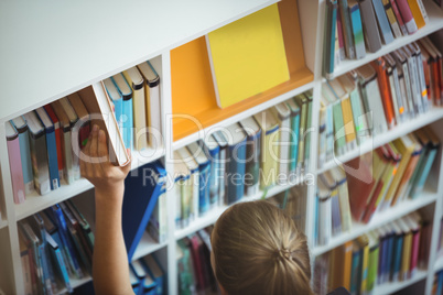 High angle view of schoolgirl selecting book from bookshelf in library