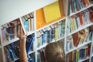 High angle view of schoolgirl selecting book from bookshelf in library