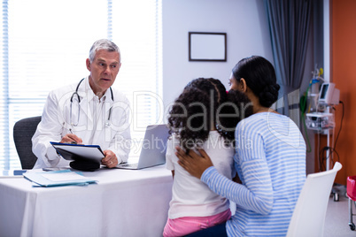 Doctor writing on clipboard while consulting patient
