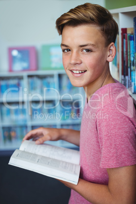 Portrait of happy schoolboy holding book in library