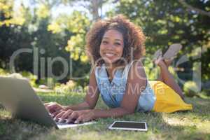 Smiling woman lying on grass and using laptop
