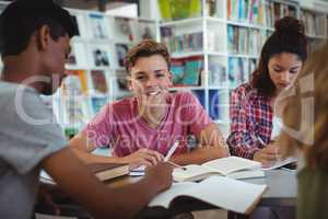 Portrait of happy schoolboy studying with his classmates in library