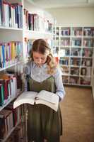 Attentive schoolgirl reading book in library