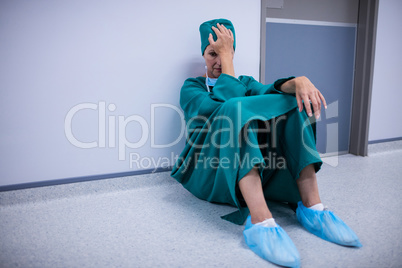 Tensed female surgeon sitting in corridor