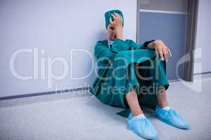 Tensed female surgeon sitting in corridor