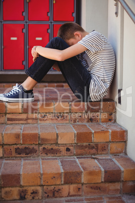 Sad schoolboy sitting on staircase