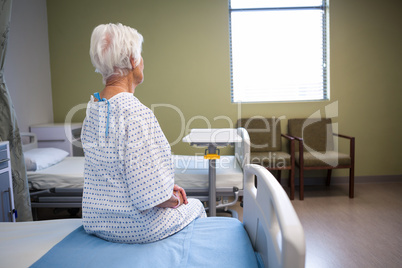 Rear-view of thoughtful senior patient sitting on bed