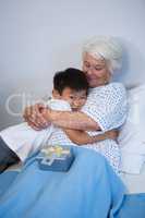 Boy giving a hug to senior patient on bed