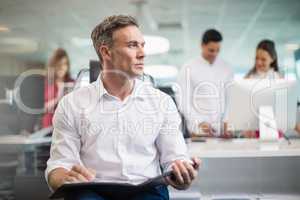 Business executive sitting on chair and writing on clipboard in office
