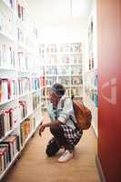 Schoolgirl selecting book from book shelf in library