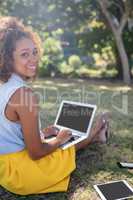 Smiling woman sitting in park and using laptop