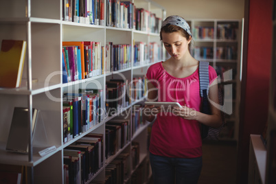 Attentive schoolgirl using digital tablet in library