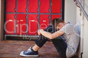 Sad schoolboy sitting in corridor