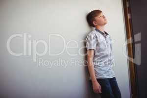 Sad schoolboy leaning head against wall in corridor