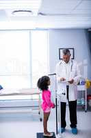 Doctor using digital tablet while measuring height of girl