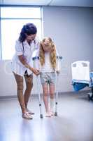 Female doctor assisting girl to walk with crutches in ward