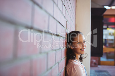 Happy schoolgirl sitting against brick wall in school campus