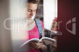 Attentive schoolgirl reading book in library