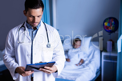 Smiling doctor writing on clipboard in ward