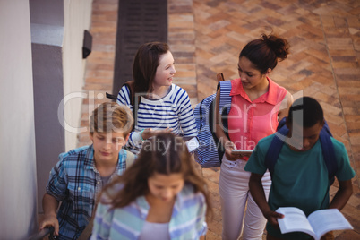 Students holding books and digital tablet walking through school campus